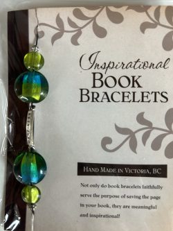 Packaged Inspirational Book Bracelet featuring dual-toned blue and green disc beads, olive accent beads, and a vertical silver metal bar engraved with "HAPPINESS" mounted on a branded backing card.